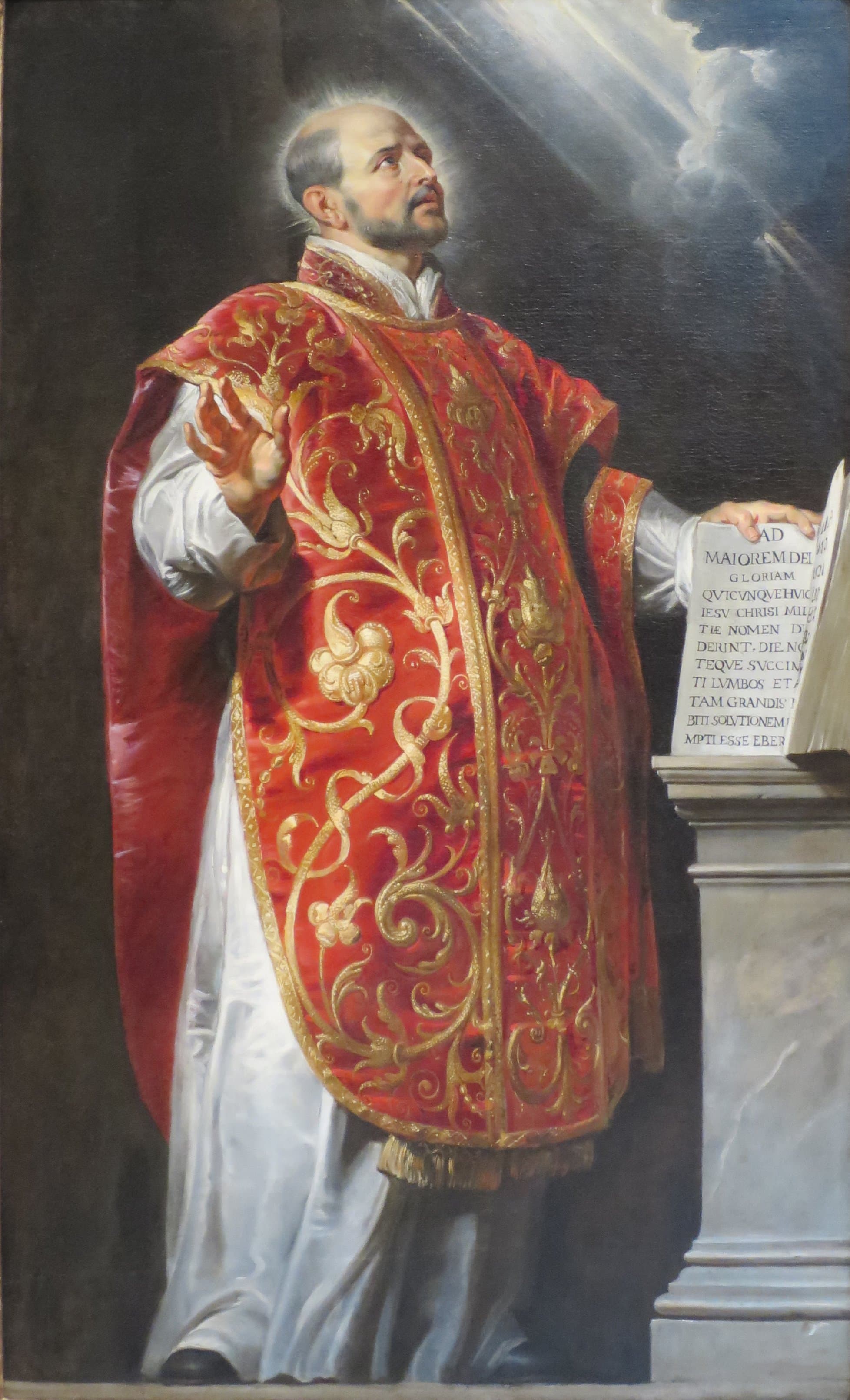 Saint Ignatius of Loyola in ornate red and gold vestments, looking upward beside an open book, painted by Peter Paul Rubens